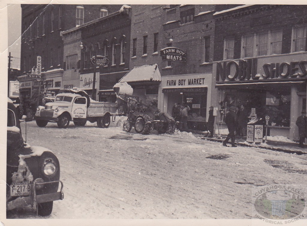 Written on the back of this photo: To Babette Robinson from Louise Moore. This is the clean up after the Thanksgiving snow storm of 1950 on Front Street in Cuyahoga Falls, Ohio. This is the block from Broad Blvd looking toward Portage Trail. L to R - Ideal Frocks, Sonny Kleins Sportshop, Siff Shoes, Singer, Isaly's (Ice Cream and Milk @ 46c), Wilfert Rexall Drugs, Valenza Bake Shop, Farm Boy Market, Nobil Shoes. The Trash can advertises "Walts 2238 State Road G.E. Television WA7113." The other sign with a picture of Santa says "Toys and Gifts at Hess and Gueutal. All buildings were long torn down in 1986. Most came down about 1969.